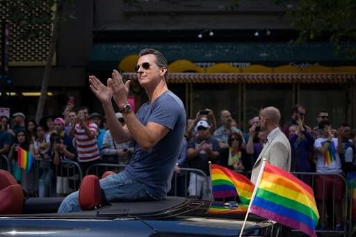 gavin newsom riding in an open convertible with pride flags