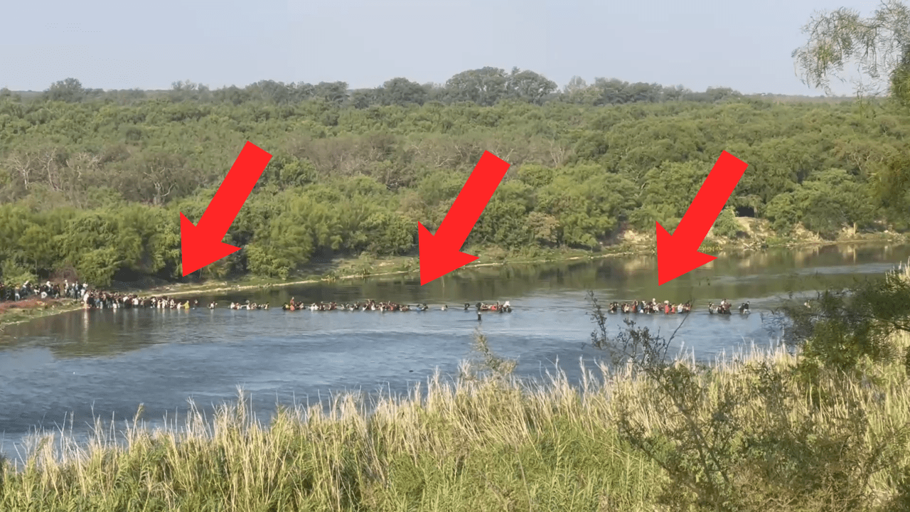 giant group of migrants wading through rio grande